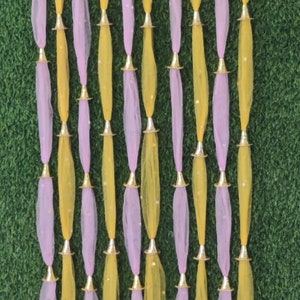 Può includere: Un set di ghirlande decorative in tessuto con fili di tulle giallo e rosa alternati. Ogni filo è decorato con accenti metallici dorati e pompon rosa in fondo.