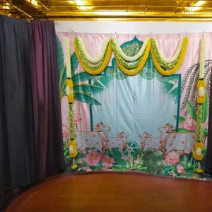 Puede incluir: Un telón de fondo rosa y azul con un diseño floral y tres vacas blancas. El telón de fondo está decorado con guirnaldas de flores amarillas y verdes.