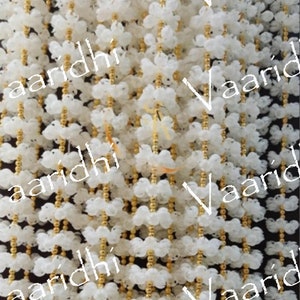 Puede incluir: Guirnalda de flores blancas con cuentas doradas. La guirnalda está hecha de muchas pequeñas flores blancas enhebradas con cuentas doradas. La guirnalda es una decoración popular para bodas y otras ocasiones especiales.