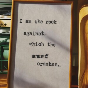 May include: A framed piece of art with a white background and black text that reads "I am the rock against which the surf crashes."