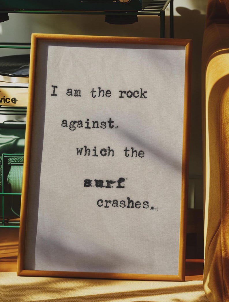 May include: A framed piece of art with a white background and black text that reads "I am the rock against which the surf crashes."
