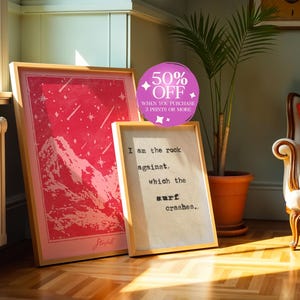 May include: Two framed prints with a pink and white color scheme. The print on the left features a pink mountain range with white stars. The print on the right features a white text quote: "I am the rock against which the surf crashes."