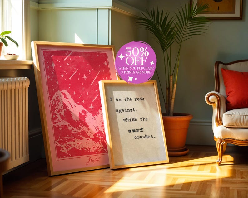 May include: Two framed prints with a pink and white color scheme. The print on the left features a pink mountain range with white stars. The print on the right features a white text quote: "I am the rock against which the surf crashes."
