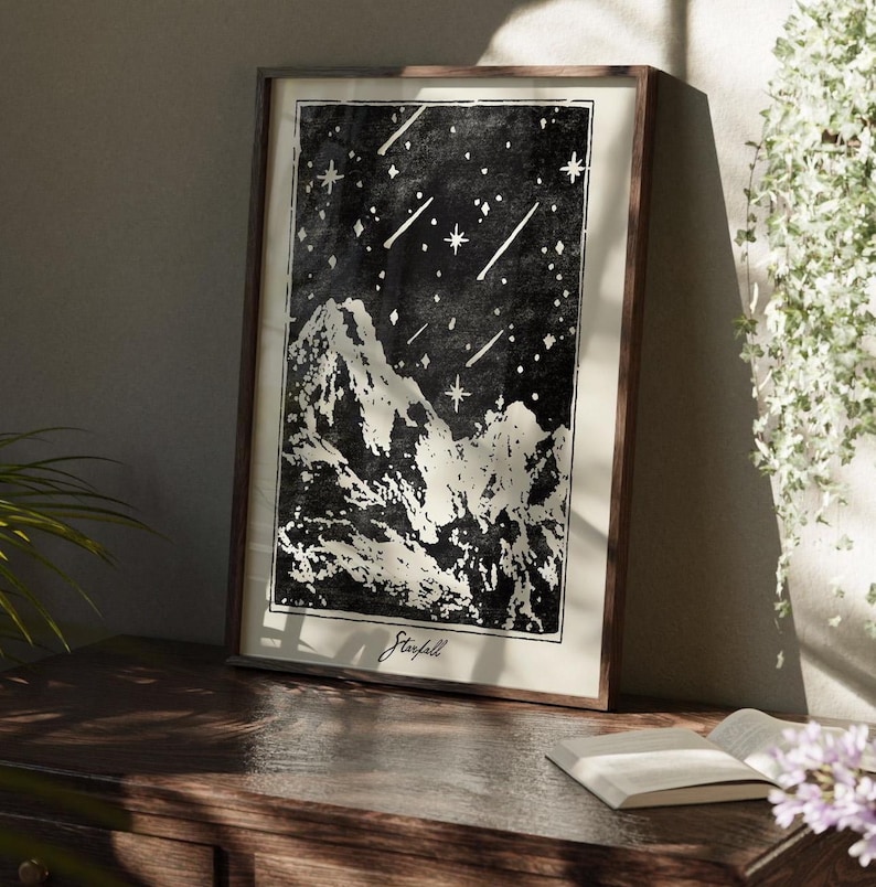 May include: Black and white print of a mountain range with shooting stars in the night sky. The print is framed in a dark wood frame and has the word "Starfall" written at the bottom.
