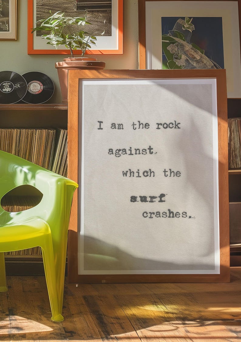 May include: A framed print with a quote in black typewriter font on a beige background. The quote reads "I am the rock against which the surf crashes..."