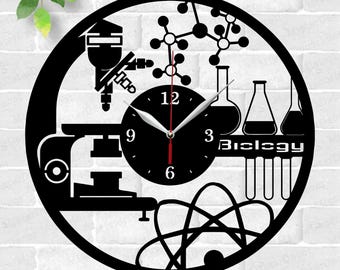 May include: Black and white laser cut clock design featuring a microscope, a DNA double helix, beakers, and test tubes. The clock face reads "Biology".