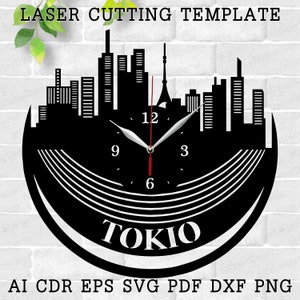 以下が含まれることがあります： 東京、日本のスカイラインを特徴とする白黒のレーザーカット時計のデザイン。時計の文字盤は、白い数字と針のある黒い背景になっています。時計の文字盤の下に「TOKIO」という文字が印刷されています。