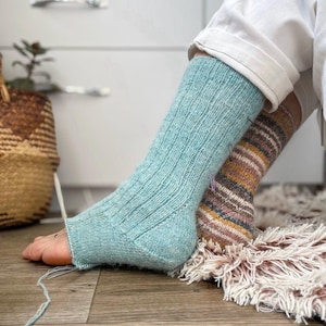 May include: A pair of knitted socks, one in a solid light blue-green color with a ribbed texture and an open toe, and the other in a multi-colored striped pattern featuring shades of brown, tan, and cream, both worn on the feet.