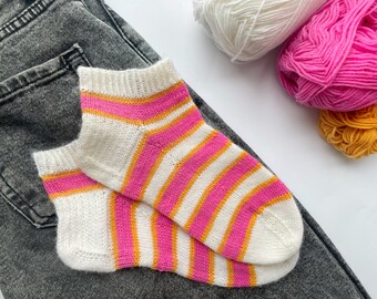 May include: A pair of white socks with pink and orange stripes. The socks are lying on a pair of gray jeans.