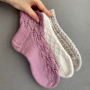 Peut inclure: Trois paires de chaussettes tricotées dans différentes couleurs et motifs. Les chaussettes sont roses, blanches et beiges. Les chaussettes ont des motifs de dentelle complexes.