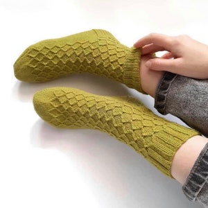 Könnte beinhalten: Ein Paar grüne Stricksocken mit einem Rautenmuster.