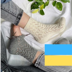 Peut inclure: Deux paires de chaussettes tricotées avec un motif ajouré. Une paire est blanche et l'autre est grise. Les chaussettes sont sur une surface blanche avec une plante verte en arrière-plan.