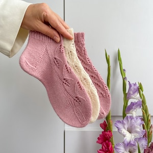 May include: Two pairs of lacy knitted socks, one pink and one white, are held together. The socks are made with a delicate, openwork stitch.