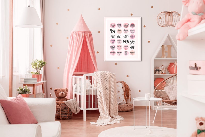 May include: A white crib with a pink canopy and a white blanket. A framed print with pink and white watercolor circles and the text "You are who God says you are" hangs on the wall. The wall is decorated with gold polka dots.