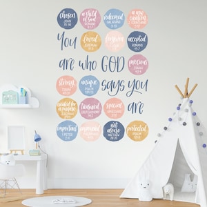 Op de afbeelding: Een witte muur met een kleurrijke set ronde stickers met bijbelteksten en inspirerende woorden. De stickers zijn in een rasterpatroon gerangschikt en hebben verschillende kleuren, waaronder roze, blauw en geel. De tekst op de stickers bevat zinnen als "Jij bent wie God zegt dat je bent", "uitverkoren", "geliefd", "verlost", "een nieuwe schepping", "sterk", "uniek", "gemaakt voor een doel", "gewaardeerd", "speciaal", "belangrijk", "bekrachtigd", "niet alleen" en "beschermd".