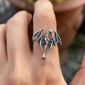 May include: A silver dragon ring with a pink gemstone. The dragon is in a flying pose with its wings spread out.