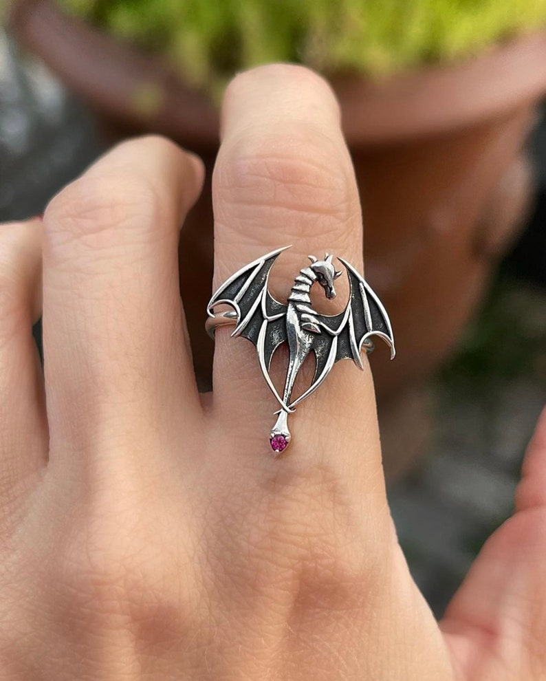 May include: A silver dragon ring with a pink gemstone. The dragon is in a flying pose with its wings spread out.