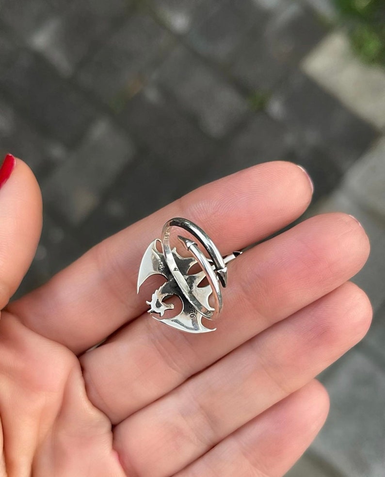 May include: A silver ring featuring a dragon design. The dragon is curled around a silver band, and the ring is open on one side.