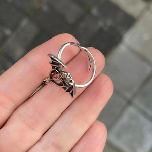 May include: A silver ring featuring a detailed design of a bat with its wings outstretched.
