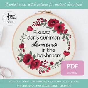 Op de afbeelding: Een kruissteekpatroon met een bloemenkrans met rode bloemen en groene bladeren rond de tekst "Please don't summon demons in the bathroom". Het patroon is voor 14-count Aida-stof en meet 9,3 x 9,6 inch (23,5 x 24,4 cm).