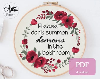 May include: A cross stitch pattern featuring a floral wreath with red flowers and green leaves surrounding the text "Please don't summon demons in the bathroom". The pattern is for 14 count Aida fabric and measures 9.3 x 9.6 inches (23.5 x 24.4 cm).