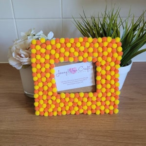 May include: A yellow and orange pom pom picture frame with a business card inside that reads "Jenny Wren Craft Handmade with Love".