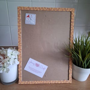 May include: A rectangular picture frame with a textured light brown border featuring a small floral pattern. The back panel is plain brown with a white instructional sticker and a white business card labeled Jenny Wren Craft.