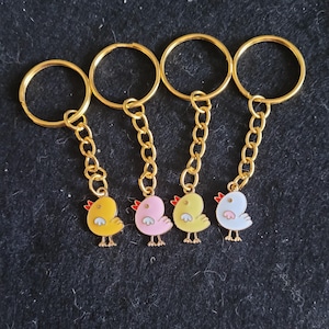 May include: Four gold keychains with small chick charms. The chicks are yellow, pink, yellow, and white with red beaks and black eyes.
