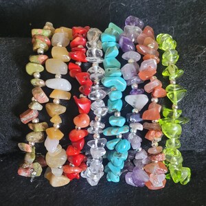 May include: A set of eight bracelets made with various semi-precious stones, including green, red, yellow, white, blue, purple, and orange. The bracelets are strung on silver wire.