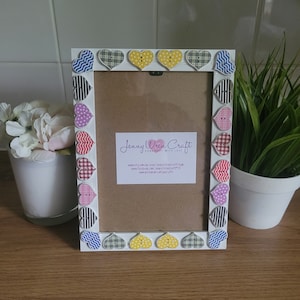 May include: White picture frame with a brown mount and a white border decorated with colourful fabric hearts. The frame has a business card with the text "Jenny Wren Craft Handmade with Love" and website information.