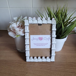 May include: White picture frame with a border of small white llama figurines. The frame has a corkboard backing and a card with the text "Jenny Wren Craft Handmade with Love" and website information.