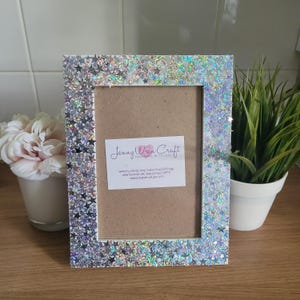 May include: A white picture frame with a silver glitter and star design. The frame has a brown cardboard backing and a small business card with the text "Jenny Wren Craft Handmade with Love" and website information.