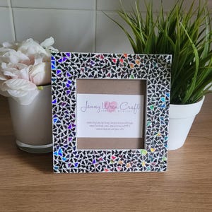 May include: A white picture frame with a black and iridescent butterfly design. The frame has a small opening for a photo and includes the text "Jenny Wren Craft Handmade with Love" and contact information.
