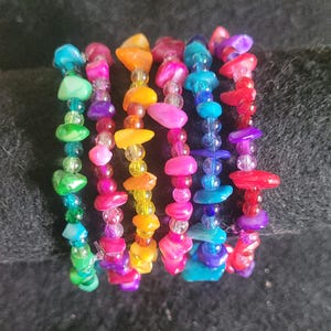 May include: A set of eight colorful bracelets made with small, iridescent beads and shell-like pieces. The bracelets are stacked on top of each other, creating a rainbow effect.
