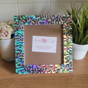 May include: A silver picture frame with a black and white patterned border made of iridescent sequins. The frame has a brown mount and a white background with the text "Jenny Wren Craft - Made with Love" and contact information.