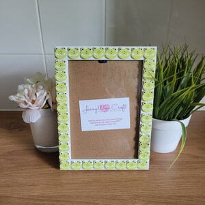 May include: White picture frame with a green frog border. The frame has a brown mat and a white background. The text "Jenny Wren Craft Handmade with Love" is visible on the mat.