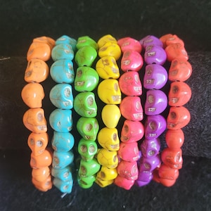May include: Seven colorful skull bead bracelets in a rainbow pattern. The bracelets are made of turquoise, green, yellow, orange, pink, purple, and blue beads.