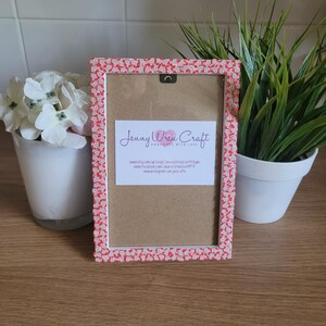 May include: A red and white picture frame with a pink and white patterned border. The frame is made by Jenny Wren Craft and is handmade with love. The frame has a brown backing and a hanging hook on the back.