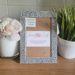 May include: A rectangular picture frame with a black and white spotted design. The frame has a brown backing and a white label with the text "REMOVE PROTECTIVE COVERING FROM BOTH SIDES". A second label reads "Jenny Wren Craft HANDMADE WITH LOVE".
