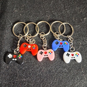 May include: Five keyrings with miniature game controller charms in black, red, pink, blue, and white. Each controller has a silver chain and a keyring. The controllers have colourful button details.