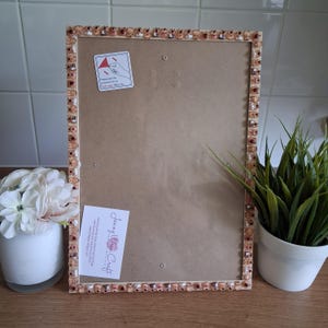 May include: A rectangular picture frame with a light wood border decorated with small, repeating miniature food-themed charms. The frame contains a clear protective sheet with a white instructional sticker and a white rectangular brand label.