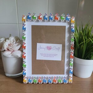 May include: White picture frame with a colorful llama border. The frame has a white mat and a clear glass front. The frame is decorated with colorful llamas around the edge. The frame is sitting on a wooden table.