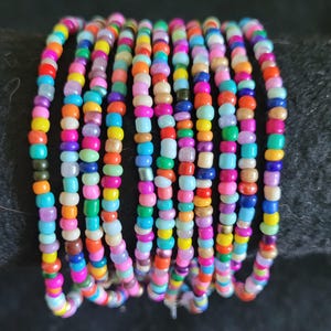 May include: A stack of colorful beaded bracelets, each with a different pattern of tiny beads in shades of pink, blue, green, yellow, orange, and purple.