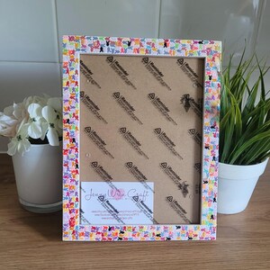 May include: A white picture frame with a colorful butterfly design. The frame is decorated with small, colorful butterflies that are arranged in a random pattern. The frame is made of wood and has a glass front. The frame is 8 inches by 10 inches.