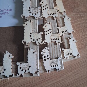 May include: Wooden llama cutouts arranged on a wooden frame. The llamas are light brown with etched details, including spots and saddle designs. The frame has a natural wood grain. The overall theme is a craft or DIY project.