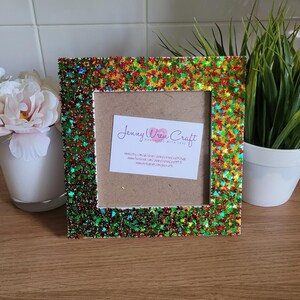 May include: A green, red, and gold glitter picture frame with a white background. The frame has a star-shaped glitter design. The frame has a business card inside with the text "Jenny Wren Craft Handmade with Love" and website information.