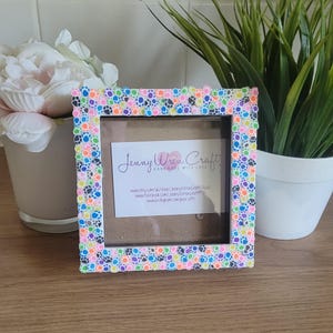 May include: A white picture frame decorated with colorful paw prints. The frame is 4x6 inches and has a clear glass front. The frame is perfect for displaying a photo of your furry friend.