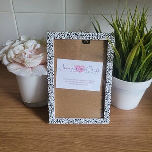 May include: White picture frame with a black and white floral design. The frame has a brown cardboard backing with a business card that reads "Jenny Wren Craft Handmade with Love" with contact information for the business.