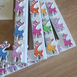 May include: A set of five white picture frames with colorful llama decorations. Each frame has a different colored llama, including pink, orange, yellow, green, and blue.