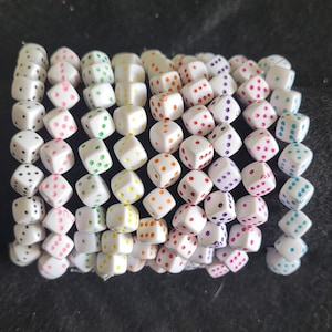 May include: A bracelet made of white dice with colourful dots. The dice are strung together to form a bracelet.